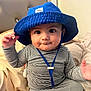 Thiago is registered to the contest to win money with this photo: baby, child, blue_hat, striped_clothing, indoor, bed, pillow, toy, face, smile, cute, chubby_cheeks, curious, sitting, headwear, infant, person, soft_lighting, home, portrait