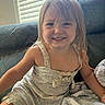Anastasia is registered to the contest to win money with this photo: child, toddler, smile, dress, blond_hair, couch, blanket, indoor, happy, face, person, young_child, home, casual_clothing, portrait, cute, sitting, window_blinds, light, cozy