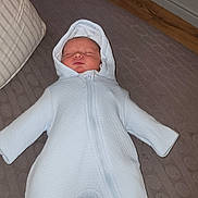 Jaxx is registered to the contest to win money with this photo: baby, infant, onesie, hooded_clothing, sleeping, blanket, floor, radiator, zipper, wood_floor, cozy, indoors, cute, child, soft_texture, peaceful, portrait, small, resting, warm