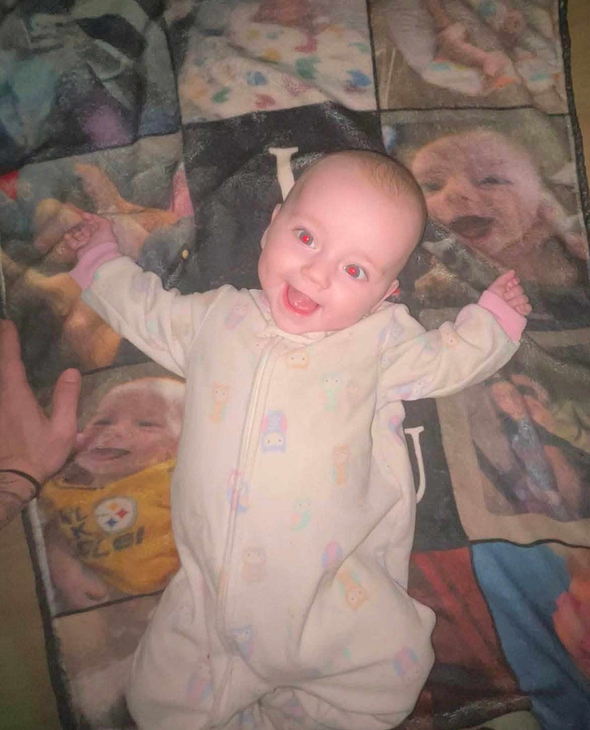 Everleigh Dawn is registered to the contest to win money with this photo: baby, infant, smiling, onesie, blanket, quilt, pattern, face, hand, red_eye, happy, lying_down, pastel_colors, indoor, portrait, child, cute, sleepwear, cozy, soft_fabric