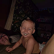 James joined the competition — help win amazing prizes! toddler, child, baby, smiling, laughing, spoon, portrait, family, adult, indoor, dim_lighting, candid, seated, diaper, bare_chested, short_hair, glasses, furniture, shelves, playful