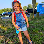 Zaylee joined the competition — help win amazing prizes! child, girl, smiling, outdoor, grass, denim_overalls, red_top, headband, bow, flip_flops, bottle, summer, sunlight, casual, playful, nature, trees, park, daytime, happy