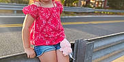 Zaylee is registered to the contest to win money with this photo: child, girl, smile, red_top, denim_shorts, plush_toy, outdoor, roadside, guardrail, sunlight, golden_hour, trees, nature, casual_pose, happy, blond_hair, shorts, footwear, summer, portrait