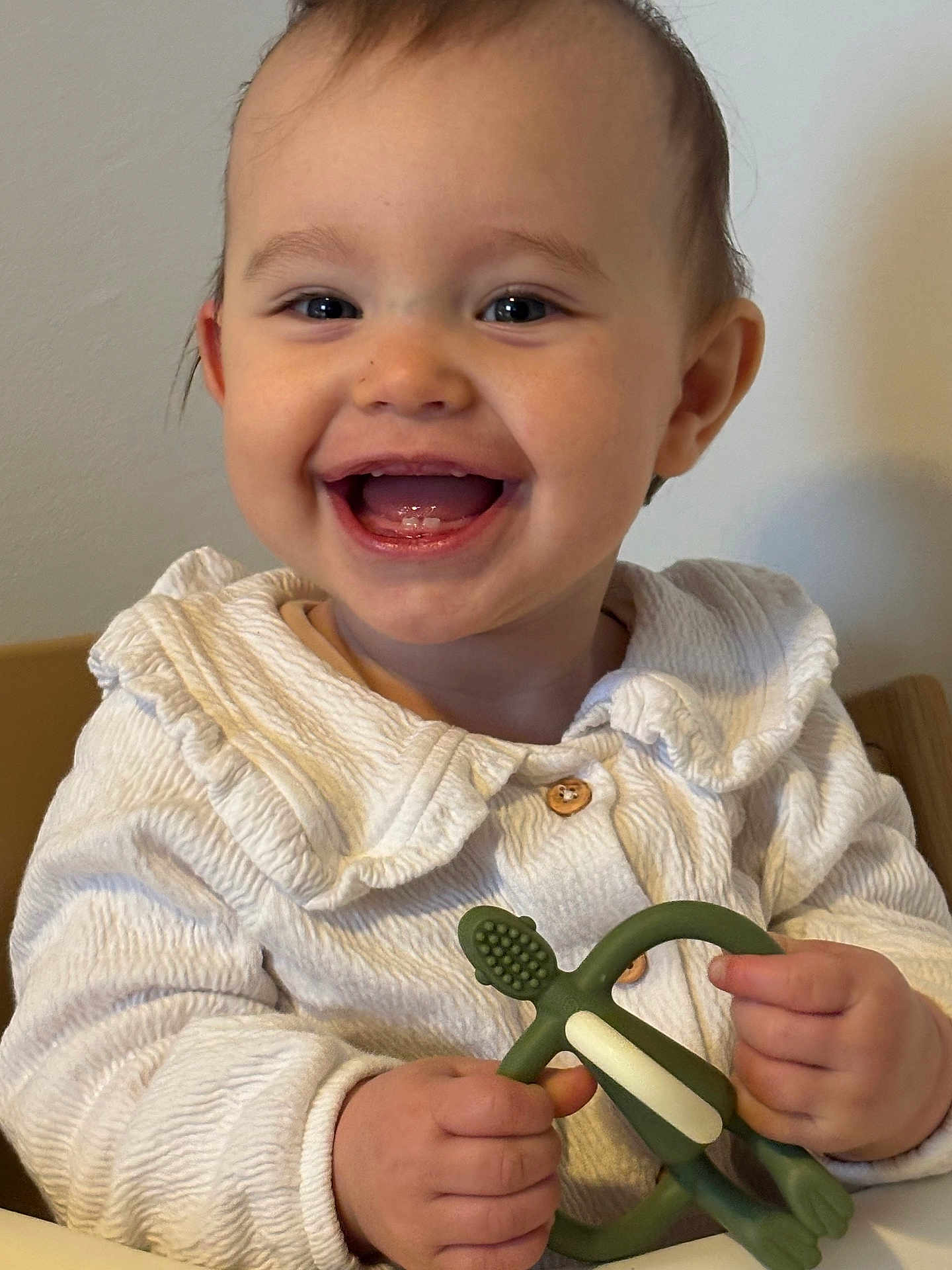 Isla is registered to the contest to win money with this photo: baby, child, smile, teether, toy, white_clothing, happy, face, hands, indoor, portrait, cute, infant, sitting, young_child, closeup, skin, person, mouth_open, eyes