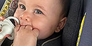 Matteo joined the competition — help win amazing prizes! baby, infant, pacifier, hand, blanket, car_seat, child, face, eyes, cute, chewing, clothing, indoors, sitting, soft_texture, warning_label, closeup, skin, head, person