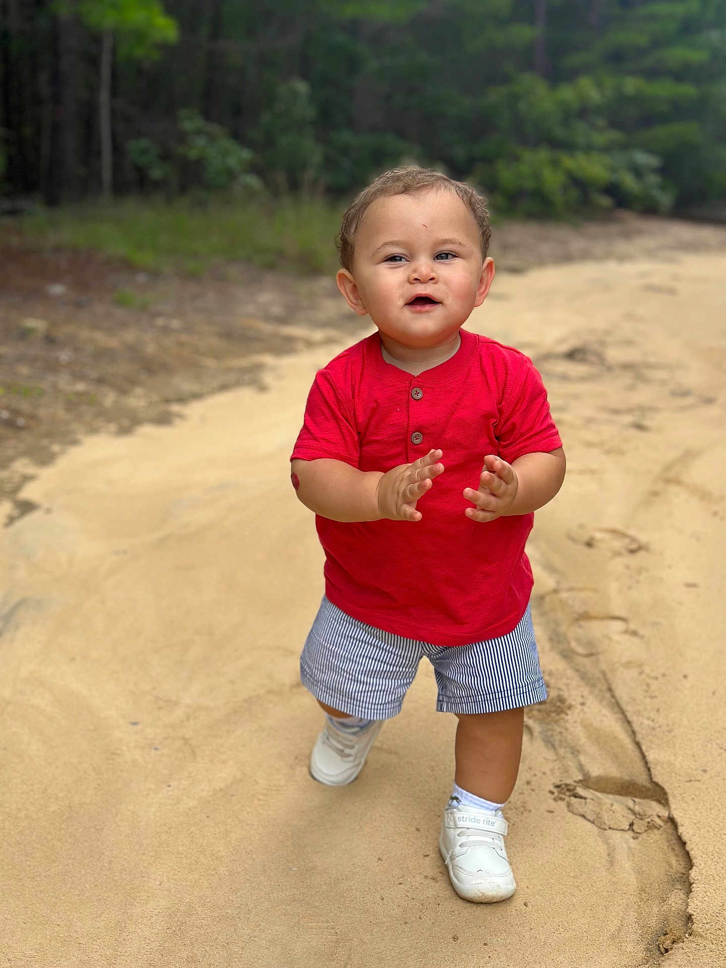 Matteo joined the competition — help win amazing prizes! toddler, child, sand, outdoor, walking, red_shirt, striped_shorts, white_shoes, clapping, nature, greenery, path, footwear, happy, young_child, casual_clothing, summer, daylight, portrait, smiling