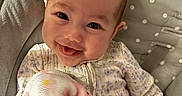 Leilani is registered to the contest to win money with this photo: baby, smiling, blanket, flamingo, polka_dot, seat, cushion, happy, child, infant, face, clothing, indoor, portrait, cozy, cute, person, head, expression, soft