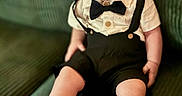 Alden-Paul is registered to the contest to win money with this photo: baby, infant, smiling, bow_tie, suspenders, red_shoes, polka_dot, couch, green_couch, happy, cute, child, indoors, portrait, sitting, clothing, footwear, person, fashion, baby_shoes