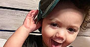 Kashton joined the competition — help win amazing prizes! child, toddler, baseball_cap, black_shirt, curly_hair, playful, tongue_out, indoor, wooden_background, smiling, person, cute, face, portrait, expressive_eyes, casual_clothing, young_child, happy, headwear, closeup