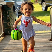 Kashton is registered to the contest to win money with this photo: toddler, child, smiling, outdoor, sunlight, porch, wooden_floor, bubbles, bucket, watermelon, footwear, slippers, clothing, curly_hair, happy, playful, person, daytime, green, background_car