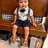 Kashton is registered to the contest to win money with this photo: toddler, child, boy, bench, wooden_bench, suspenders, bow_tie, floral_shirt, shorts, sandals, curly_hair, indoor, floor_tiles, boxes, checkered_wallpaper, seated, portrait, cute, fashion, smiling