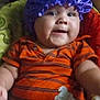 baby, baby_seat, child, chubby_cheeks, closeup, cute, fan, furniture, happy, headwear, home, indoor, infant, orange_outfit, person, portrait, purple_bonnet, seat_belt, smiling, striped_clothing