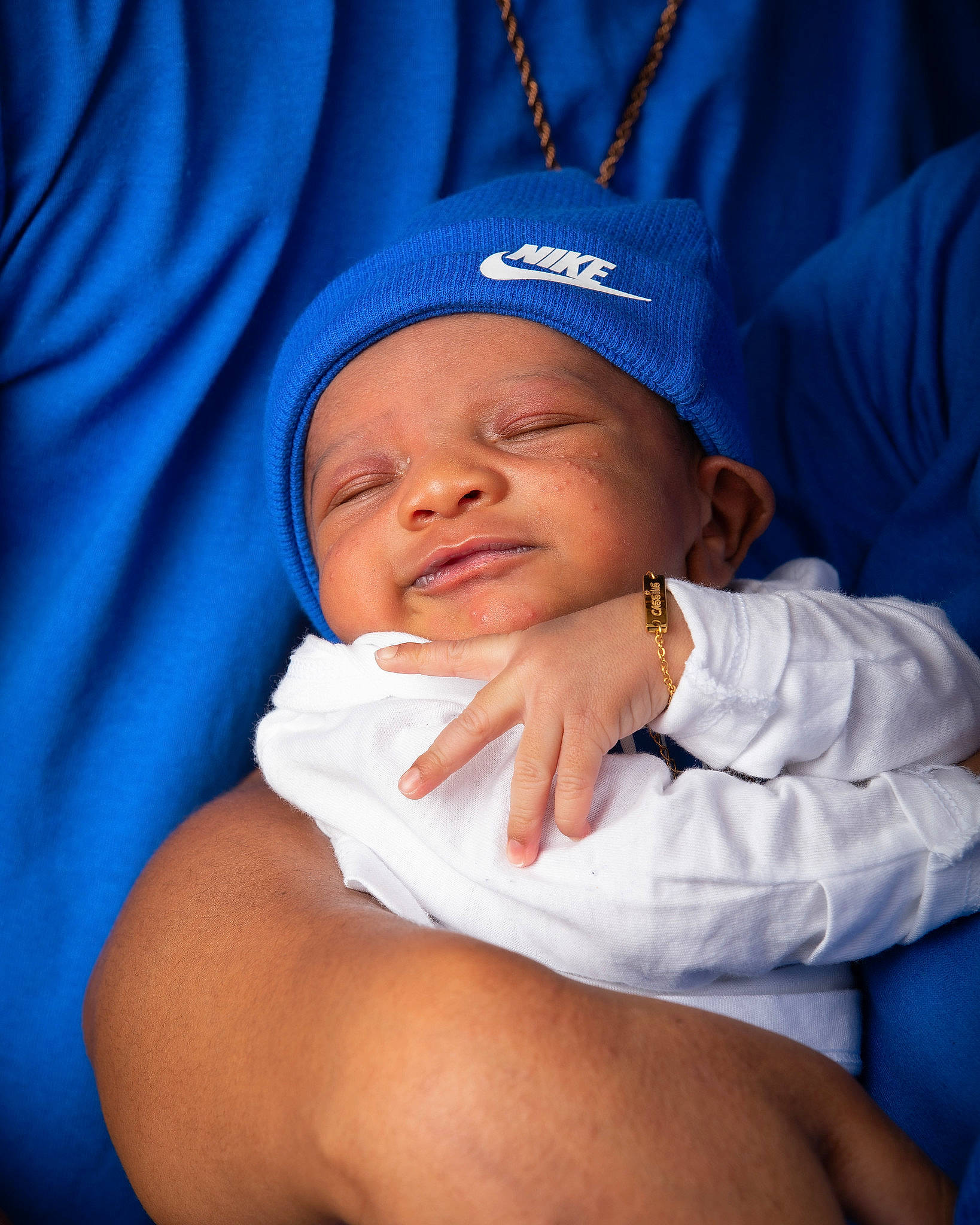 Cassius is registered to the contest to win money with this photo: arm, baby, blue, cap, cheek, comfort, eye, eyebrow, finger, gesture, hand, happy, hat, head, headwear, human_body, lip, mouth, person, purple