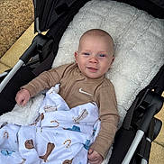 Greyson is registered to the contest to win money with this photo: baby, stroller, blanket, infant, smiling, cozy, outdoor, clothing, cute, child, face, happy, portrait, soft, patterned_blanket, warm, baby_clothes, cushion, seat, blue_eyes