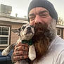 Chaos is registered to the contest to win money with this photo: animal, beard, bow_tie, clothing, dog, face, furniture, hand, hat, holding, house, man, outdoor, patio, person, pet, puppy, smile, tattoo, window