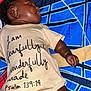 baby, infant, onesie, clothing, text_on_clothing, lying_down, hand, face, skin, blanket, pattern, colorful, peaceful, indoors, newborn, child, closeup, portrait, cute, toddler