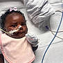 baby, infant, female, pink_bib, mittens, feeding_tube, hospital, lying_down, curly_hair, bow, white_background, medical_tape, closeup, cute, patient, newborn, healthcare, soft_lighting, portrait, child