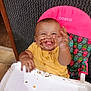 baby, child, high_chair, chocolate, messy, smiling, happy, yellow_shirt, face, hand, food, indoor, seat, colorful, pattern, playful, person, young_child, dirt, fun