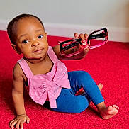 Kiley is registered to the contest to win money with this photo: toddler, child, pink_top, blue_leggings, red_carpet, glasses, holding, sitting, cute, indoor, playing, baby, portrait, smiling, young_child, hand, foot, expression, person, floor