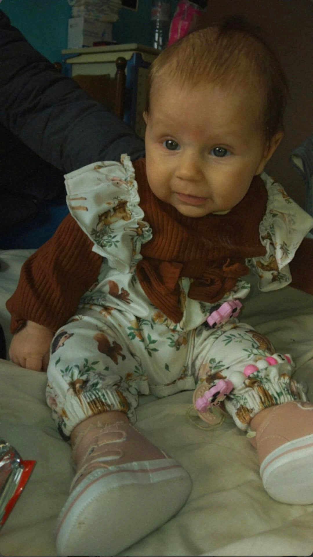 Inaya a rejoint le concours — aidez-le/la à gagner de superbes lots ! baby, infant, child, clothing, shoes, bed, indoors, person, cute, smile, sitting, patterned_clothes, pink, white, brown, young, face, expression, toy_clip, soft_lighting