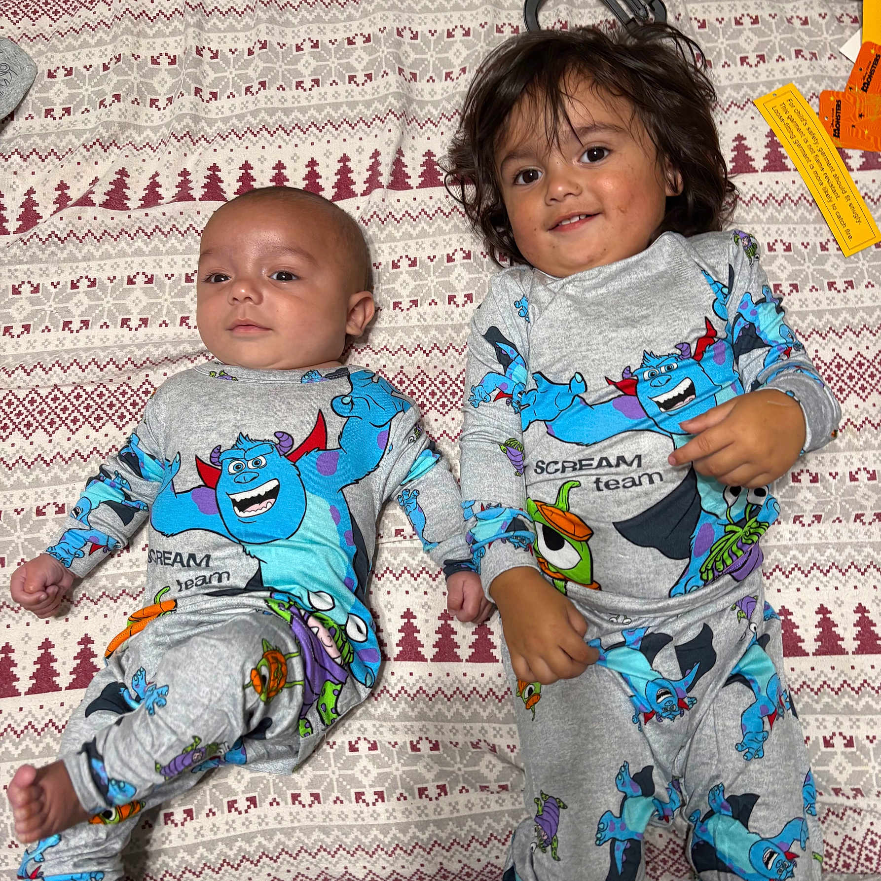 Leonardo is registered to the contest to win money with this photo: baby, toddler, siblings, children, portrait, smiling, lying_down, blanket, bedroom, pajamas, matching_outfits, monster_print, cartoon, patterned_fabric, infant, young_child, faces, indoor, family, photography