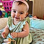 baby, child, infant, smiling, headband, pink, dress, green, toy, book, fabric, elephant_pattern, cushion, indoor, cute, happy, small_hands, face, person, play