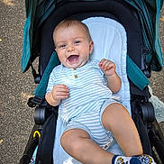 Daors is registered to the contest to win money with this photo: baby, child, stroller, smiling, happy, onesie, socks, bicycle_design, outdoor, pavement, infant, seat, baby_clothing, cute, person, legs, hand, head, face, daylight