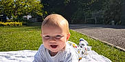 Daors is registered to the contest to win money with this photo: baby, child, blanket, grass, outdoor, sunlight, smiling, happy, nature, sky, trees, park, crawling, clothing, infant, daytime, person, play, greenery, cute