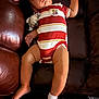 baby, sleeping, onesie, striped_clothing, plush_toy, couch, leather, furniture, infant, child, relaxed, footwear, sock, indoor, peaceful, resting, cute, young_child, person, home