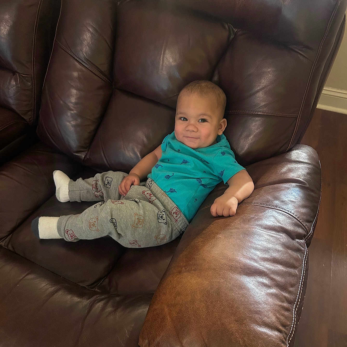 Xane joined the competition — help win amazing prizes! blue_shirt, candid, child, comfortable, cute, furniture, grey_pants, happy, home, indoors, leather_couch, living_room, portrait, relaxed, seated, smiling, socks, toddler, wooden_floor, young_child
