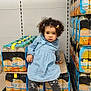Alya a rejoint le concours — aidez-le/la à gagner de superbes lots ! child, toddler, girl, curly_hair, blue_dress, leggings, sneakers, grocery_store, shelves, juice_packs, pallet, sitting, face, serious_expression, hair_clips, floor_tiles, packaged_drinks, plastic_wrap, aisle, cardboard