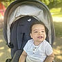 Owen a rejoint le concours — aidez-le/la à gagner de superbes lots ! baby, casual_clothing, child, curly_hair, daylight, greenery, happy, nature, outdoor, park, person, relaxing, seat, shade, smile, stroller, sunlight, toddler, white_shirt, young_child