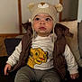 cartoon_print, child, couch, cute, expression, eyes, face, hat, indoor, knit_hat, lion_print, pants, pom_poms, portrait, sitting, socks, toddler, vest, white_sweater, young_child