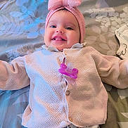 Samia participe au concours pour gagner de l'argent avec cette photo : baby, infant, smiling, pink_bow, headband, pacifier, sweater, pajamas, bed, stuffed_animal, toy, lying_down, happy, cute, child, face, tongue_out, indoor, patterned_bedspread, cozy