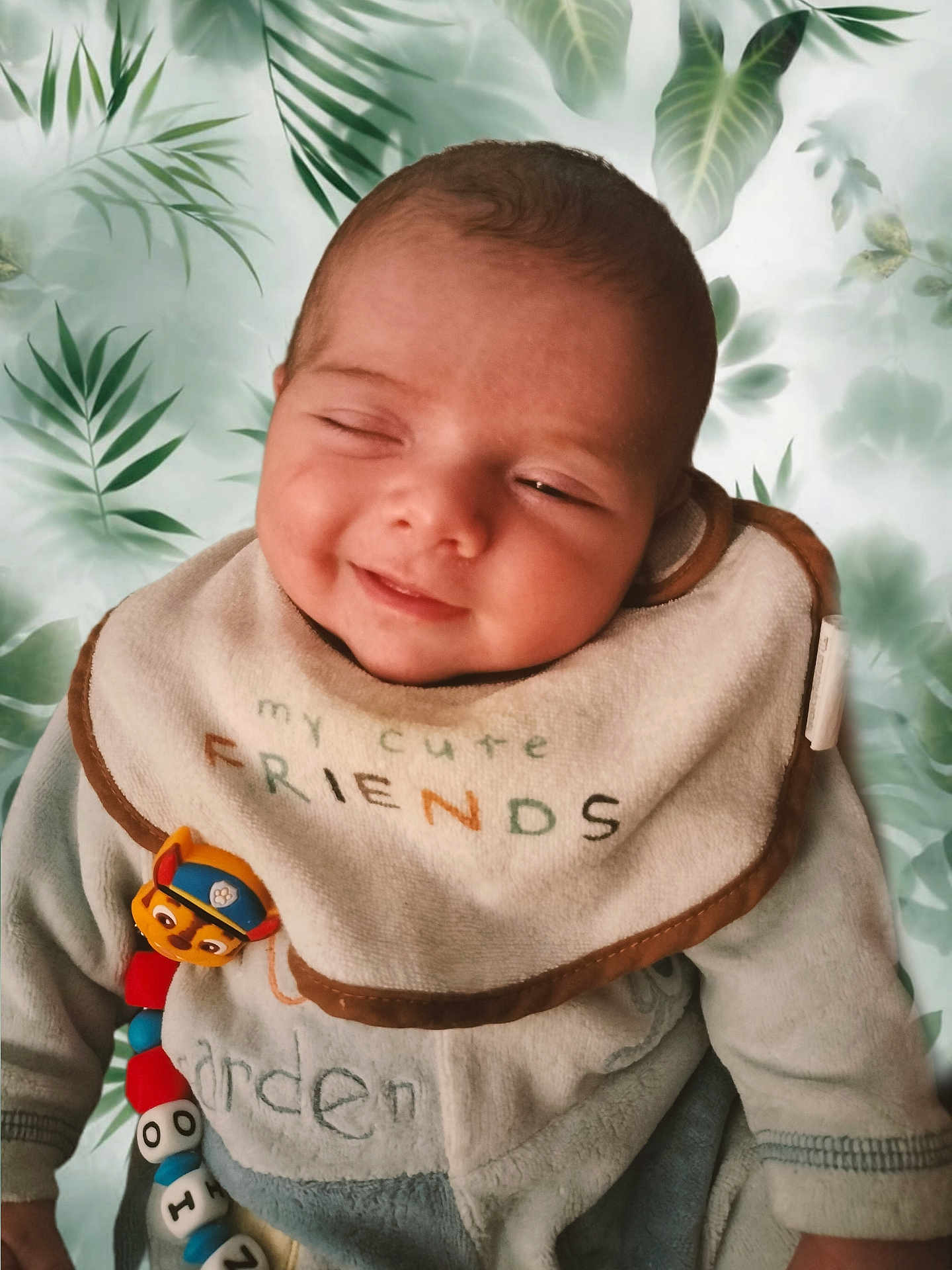 Ezio participe au concours pour gagner de l'argent avec cette photo : baby, infant, newborn, smile, sleepy, bib, toy, toy_clip, onesie, clothing, chubby_cheeks, face, head, portrait, close_up, green_leaf_background, leaf_pattern, soft_texture, indoor, cute