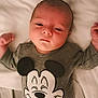 Ezio participe au concours pour gagner de l'argent avec cette photo : baby, infant, newborn, mickey_mouse, onesie, clothing, bed, bedding, sheet, portrait, face, head, eyes, hands, lying_down, indoor, home, person, cute, sleepy
