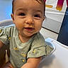 Janali joined the competition — help win amazing prizes! baby, child, high_chair, food, face, smiling, indoor, clothing, short_sleeves, curly_hair, banner, window, plant, table, person, toddler, cute, expression, home, portrait