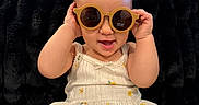 Janali joined the competition — help win amazing prizes! baby, black_background, bright_lighting, child, clothing, cute, floral_pattern, hands_up, happy, indoor, infant, person, playful, plush_blanket, portrait, round_sunglasses, seated, smiling, sunglasses, white_dress