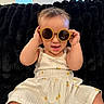 Janali joined the competition — help win amazing prizes! baby, child, sunglasses, white_dress, floral_pattern, smiling, cute, indoor, plush_blanket, black_background, playful, happy, seated, infant, round_sunglasses, clothing, person, portrait, bright_lighting, hands_up