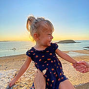 Luciana participe au concours pour gagner de l'argent avec cette photo : child, girl, smiling, sunset, beach, ocean, rock, holding_hands, blue_dress, ponytail, outdoor, water, sand, sky, nature, happy, person, sunlight, vacation, holiday