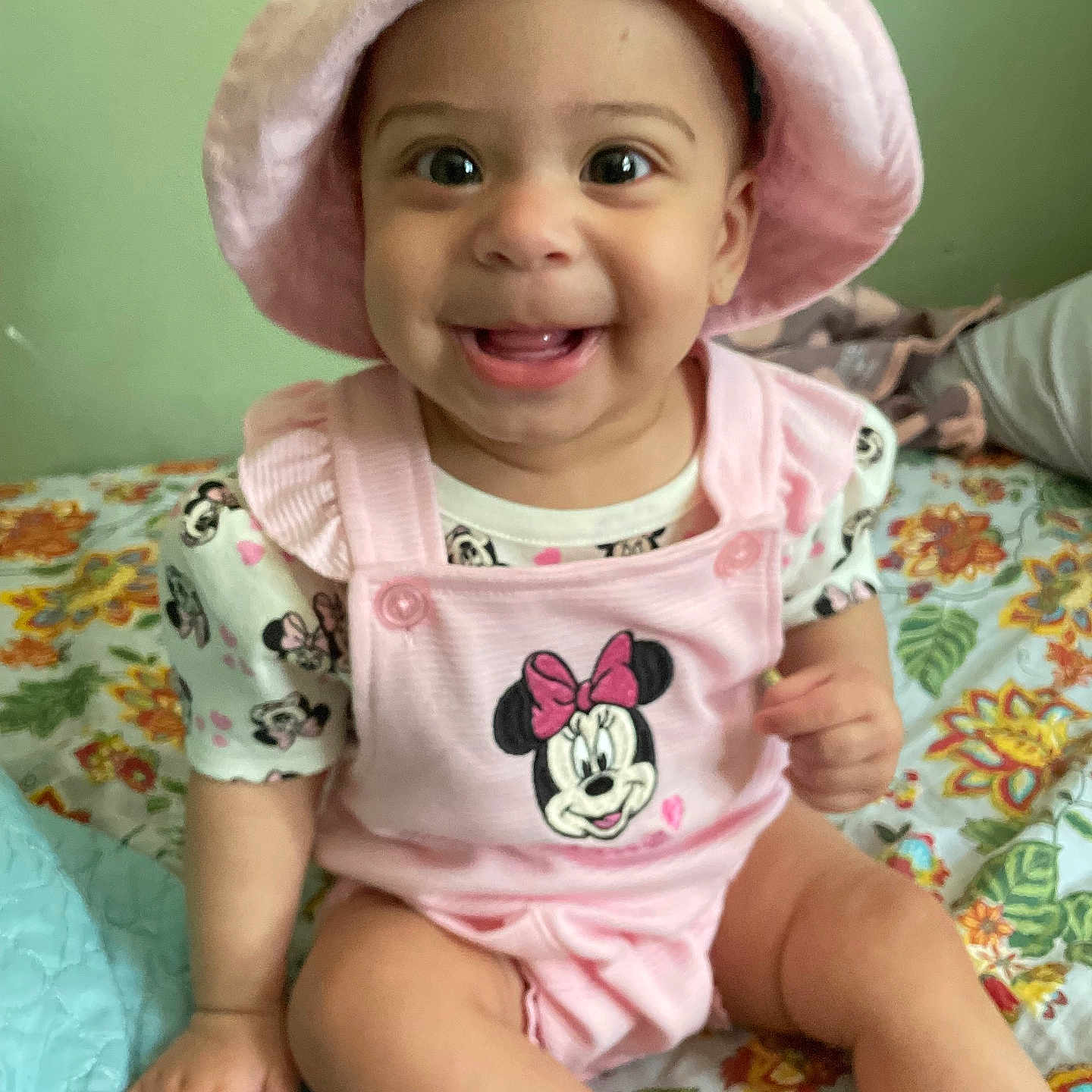 Elizabeth joined the competition — help win amazing prizes! baby, child, infant, smiling, pink_hat, pink_clothing, minnie_mouse, sitting, bedspread, floral_pattern, cute, happy, indoors, person, face, headwear, clothing, young_child, playful, portrait