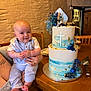 baby, child, infant, cake, birthday_cake, celebration, blue, white, cross, decoration, table, wooden_furniture, smile, holding, person, indoor, plate, flower_decoration, hand, tattoo