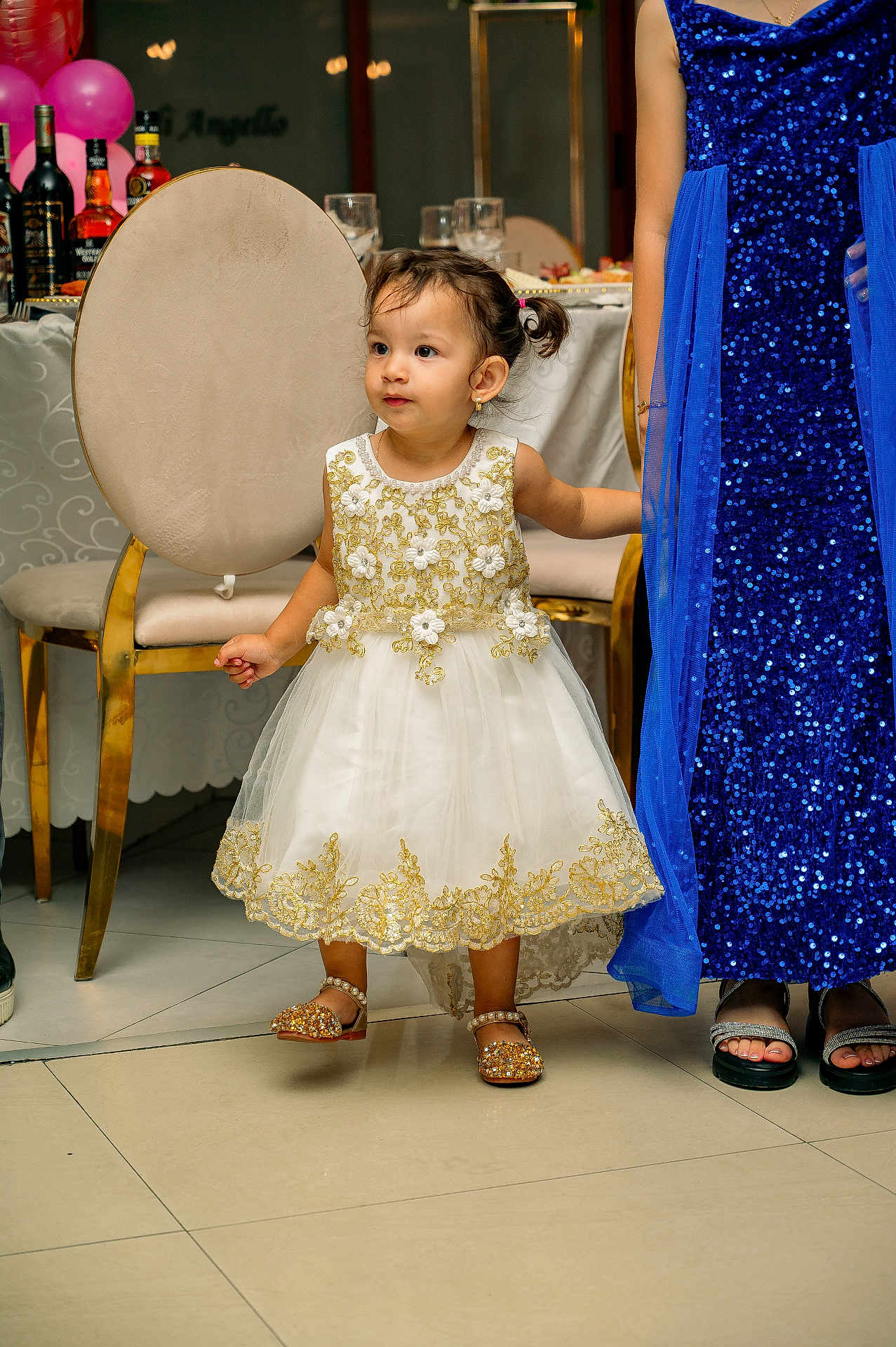 Naissa participe au concours pour gagner de l'argent avec cette photo : toddler, child, dress, party, indoor, balloons, bottle, glass, table, chair, floor, footwear, adult, gown, sparkle, celebration, people, event, gold, white