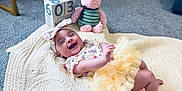 Sophia is registered to the contest to win money with this photo: baby, infant, smile, tutu, headband, quilt, plush_toy, teddy_bear, calendar_blocks, carpet, indoor, child, cute, happy, lying_down, fabric, soft_toy, decor, playtime, person