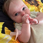Emma is registered to the contest to win money with this photo: baby, infant, pacifier, hand, face, skin, blanket, sunflower, pattern, lying_down, cute, close_up, child, young, human, expression, indoors, soft_light, comfort, resting