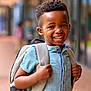 child, boy, smiling, backpack, blue_shirt, short_sleeves, outdoor, portrait, happy, standing, school, casual_clothing, person, young, african_american, daylight, urban, focus, blurred_background, positive_emotion