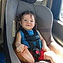 blue_shirt, car_interior, car_seat, child, face, foot, hair, hand, happy, indoors, person, playful, red_shorts, safety, seat_cushion, seatbelt, smile, sunlight, toddler, window