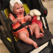 Néllya participe au concours pour gagner de l'argent avec cette photo : baby, bow, child, cute, floor, footwear_absent, happy, headband, indoor, infant, joyful, orange_clothing, person, plush_bunny, portrait, seatbelt, sitting, smiling, stroller, toy