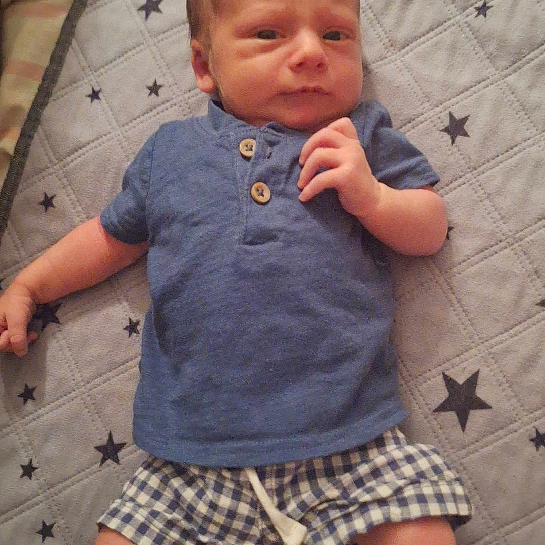 Damien is registered to the contest to win money with this photo: baby, child, infant, lying_down, portrait, blue_outfit, plaid_shorts, quilt, blanket, stars, indoors, bed, baby_fashion, short_hair, hands, feet, facial_expression, photography, home, cute
