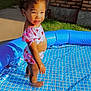anklet, brick_wall, child, concrete, curly_hair, cute, daytime, grass, happy, inflatable_pool, outdoor, play, side_view, smiling, summer, sunlight, swimsuit, toddler, truck, water